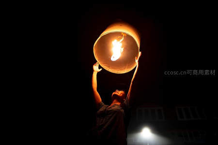 夜空中双手托举燃烧孔明灯的剪影，温暖火光映照希望与祈愿