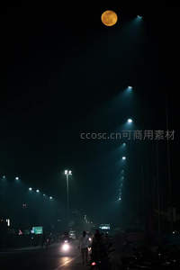 夜幕下橙月高悬，街灯如星链延伸，行人与车流穿行于朦胧雾霭中