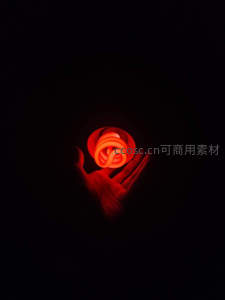 黑暗中手掌托举发光螺旋节能灯，红光映照指尖轮廓