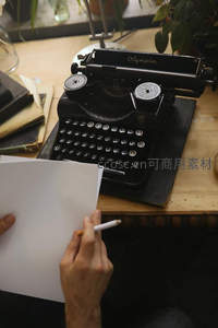手持白纸与铅笔凝视老式Olympia打字机，准备开启一段文字旅程