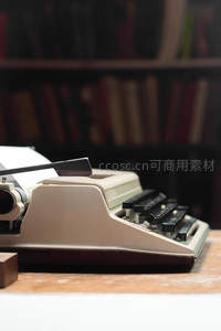 米白色老式打字机静置于木质书桌，背景书架朦胧怀旧